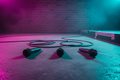 Three black wireless microphones lying parallel on concrete warehouse floor with magenta-cyan stage lighting