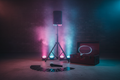 PA speaker on tripod with uplights, prop trunk and wireless mic on concrete warehouse floor with magenta-cyan stage lighting