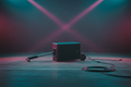 Black 10-inch subwoofer cabinet with retractable handle on concrete warehouse floor with magenta-cyan stage lighting