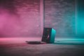 Black studio monitor speaker on concrete warehouse floor with magenta-cyan stage lighting