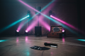 Full garage party rig spread on concrete warehouse floor with PA, subwoofer, moving heads, prop trunk and request cards in magenta-cyan stage lighting