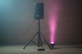 Black PA speaker on tripod with wireless mic and LED light on concrete warehouse floor with magenta-cyan stage lighting